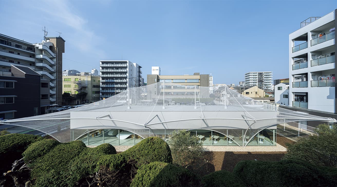 ホワイトキューブの長方形の建物全体を有機的に包み込む雲のようなメッシュ。メッシュを支えるアーチ状の鉄骨フレームは内部建築を支える鉄骨フレームと連動し、耐震性能の確保にも役立っている。