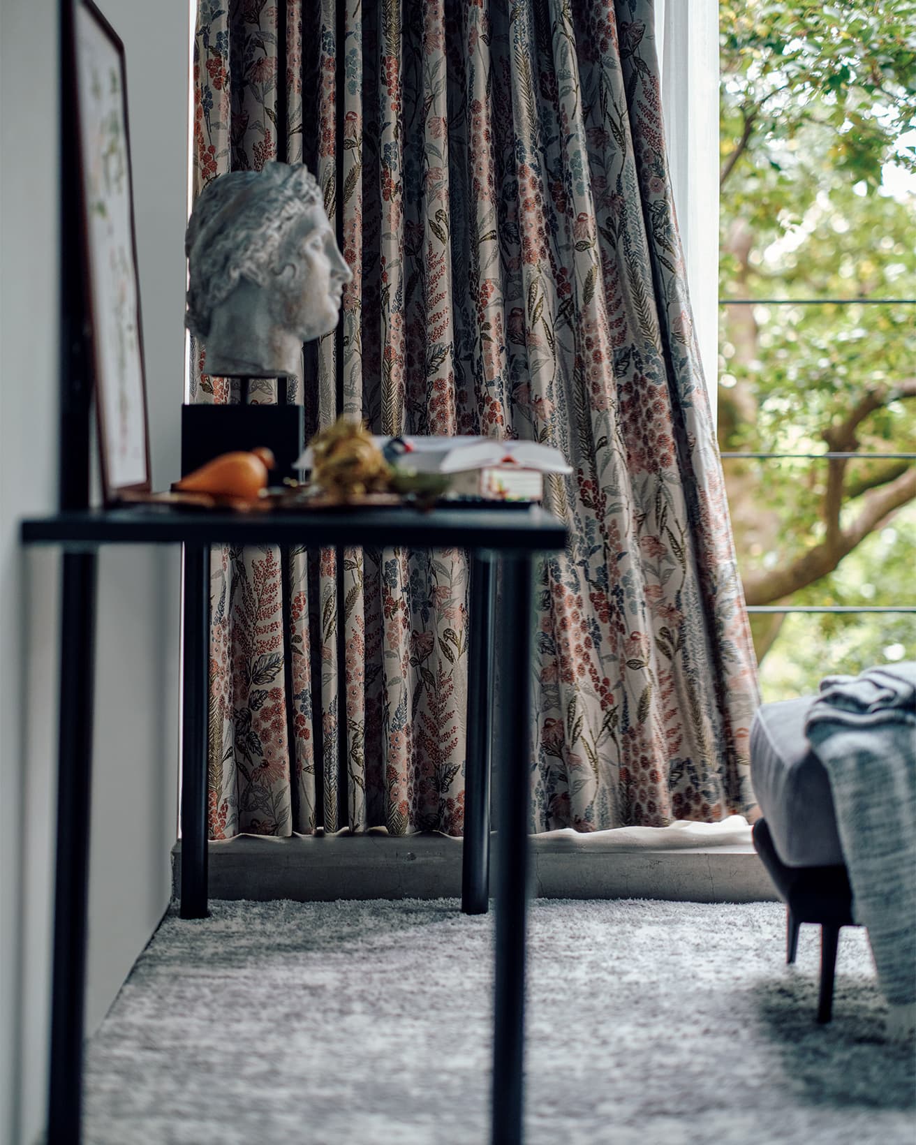 同じ柄のカーテンがさまざまな雰囲気の空間で美しい暮らしを演出してくれるのも、ジャカードカーテンならではの魅力といえる。オーダーカーテン1.5倍ヒダ(W176×H213㎝×2枚)30,900円、オーダーレースカーテン2倍ヒダ(W176×H212㎝×2枚)33,900円、フリーカバー2,990円、スツール(W60×D50×H43㎝)19,990円、アクセントラグ(約133×190㎝)17,990円、組み合わせデスク各種:天板(W140×D59×H3㎝)7,000円、脚2Pセット(2個使用)(W9×D9×H69㎝)2,000円(以上ニトリ)。テーブルなどに置かれた彫像、書籍、置物などはスタイリスト私物。